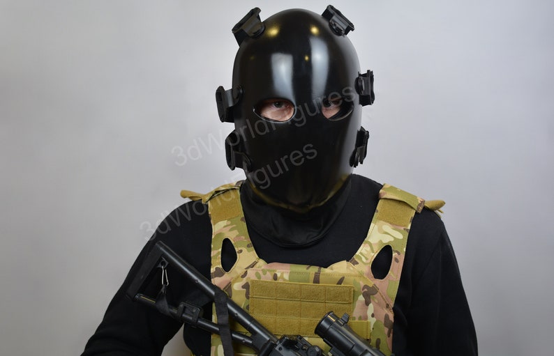 May include: A person wearing a black tactical helmet with a face shield and a camouflage vest. They are holding a black rifle with a scope.