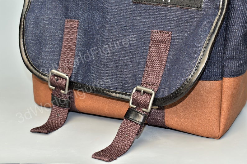 May include: A blue denim messenger bag with brown straps and silver buckles. The bag has a brown leather trim and a brown fabric bottom.