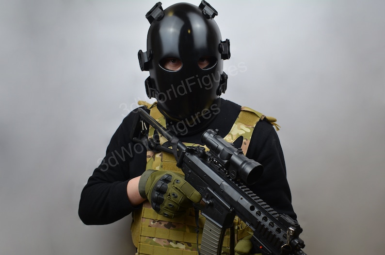 May include: A person wearing a black tactical helmet and a camouflage vest holds a black rifle with a scope.