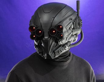 May include: A black futuristic helmet with six red glowing eye-like lights. The helmet has a complex design with tubes, antennas, and other mechanical details. The person is wearing a black turtleneck.