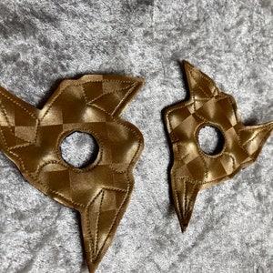 May include: Two gold-coloured fabric shapes with a chequered pattern and a hole in the centre. The shapes are in the form of a five-pointed star.
