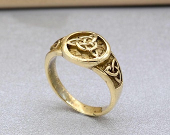 May include: A gold ring featuring a Celtic knot design. The knot is centrally positioned on the ring and is encircled by a raised border. The ring band is also adorned with Celtic knots.