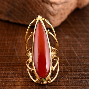 以下が含まれることがあります： 繊細な透かし模様にセットされた、大きな涙型の赤い宝石がついたゴールドのリングです。