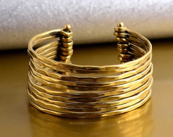 May include: A gold-toned metal cuff bracelet with a hammered finish. The bracelet is made of multiple bands stacked on top of each other.