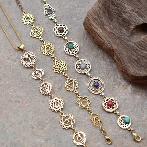 May include: Three gold necklaces featuring chakra symbols and gemstones. The necklaces are of varying lengths and styles, including a pendant with an Om symbol.
