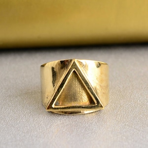 May include: A gold-toned ring with a triangular design. The ring is wide and has a smooth, polished finish.