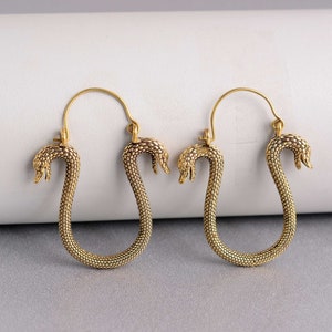 Könnte beinhalten: Ein Paar goldfarbene Schlangen-Creolen. Die Ohrringe sind aus Metall und haben ein strukturiertes Schlangendesign. Die Schlangenköpfe sind nach vorne gerichtet und die Ohrringe hängen an einem Ring.