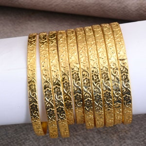 May include: A set of ten gold-tone bangles with a floral design. The bangles are stacked on top of each other.