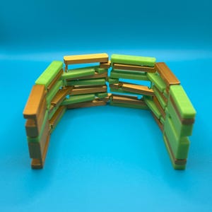 May include: A wooden bracelet with a curved design. The bracelet is made of small rectangular blocks in shades of green, gold, and brown. The background is a solid blue.
