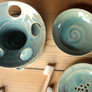 Puede incluir: Un juego de tres accesorios de baño de cerámica en un esmalte azul y verde. El juego incluye un portacepillos de dientes con cinco agujeros, un plato pequeño con un diseño de espiral y un plato más grande con un agujero de drenaje.