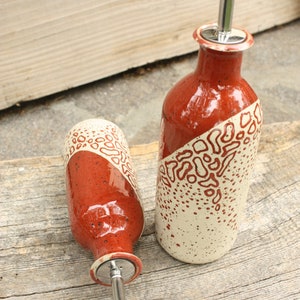 May include: Two ceramic oil and vinegar bottles with red and white speckled glaze and stainless steel pour spouts.