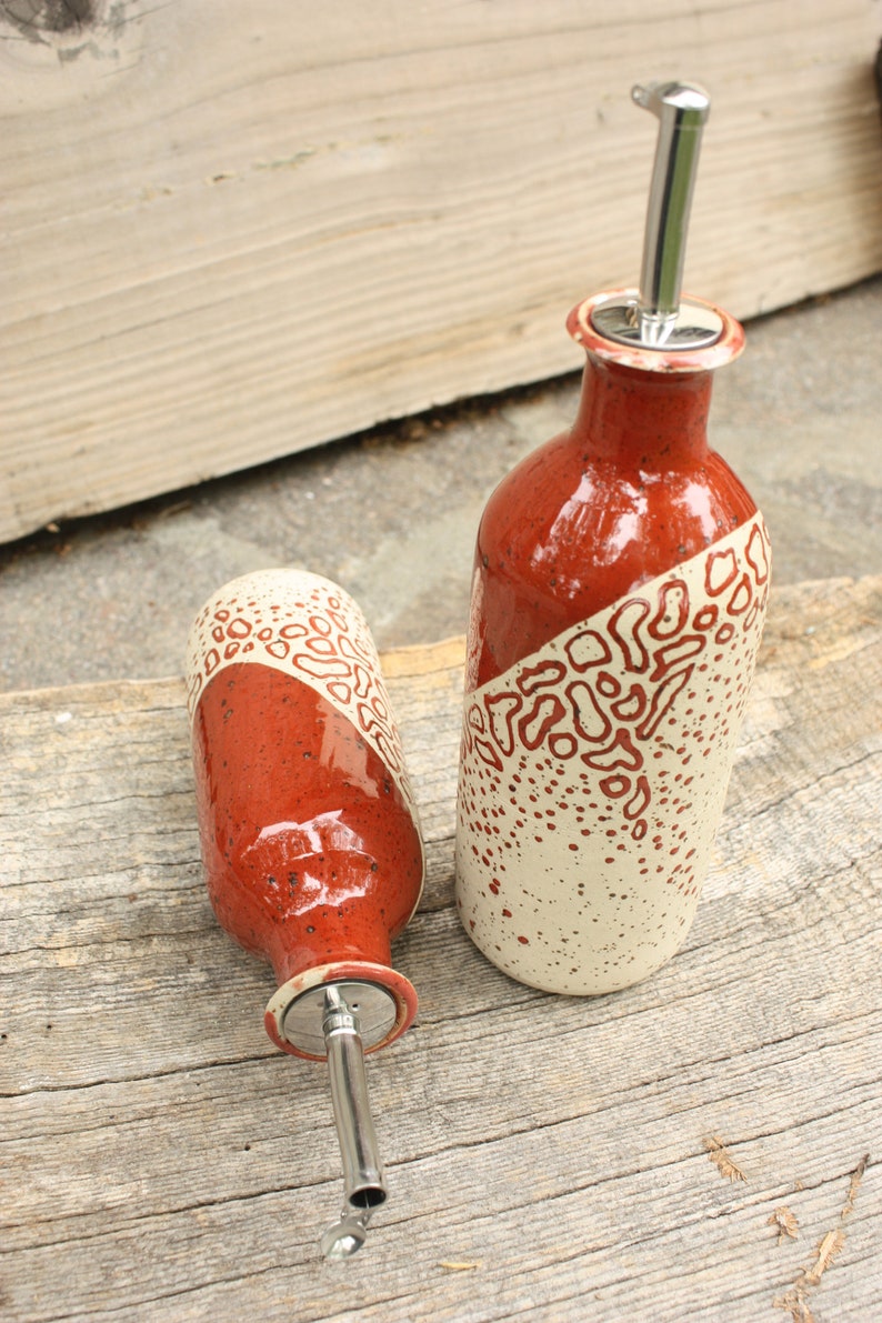 May include: Two ceramic oil and vinegar bottles with red and white speckled glaze and stainless steel pour spouts.