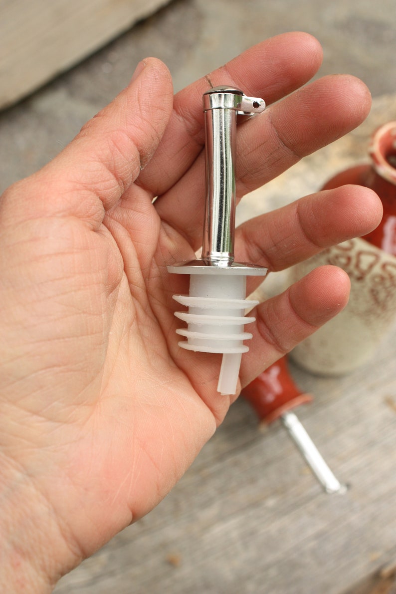 May include: A silver bottle pourer with a white plastic spout. The pourer has a lever to control the flow of liquid.