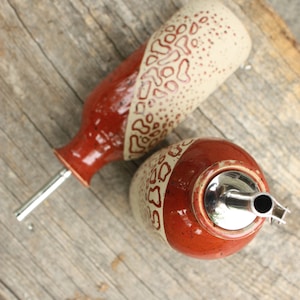 May include: Two ceramic oil and vinegar bottles with red and white speckled glaze and a geometric pattern. The bottles have metal pour spouts.