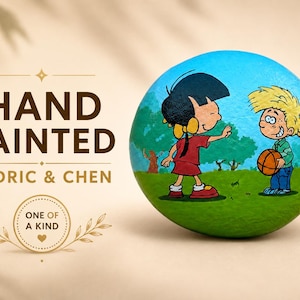 May include: A round, hand-painted stone featuring a colorful cartoon illustration of two children, Cedric and Chen, standing on a green grassy field with a blue sky background. The boy holds a basketball. Text on the left reads HAND PAINTED CEDRIC & CHEN.