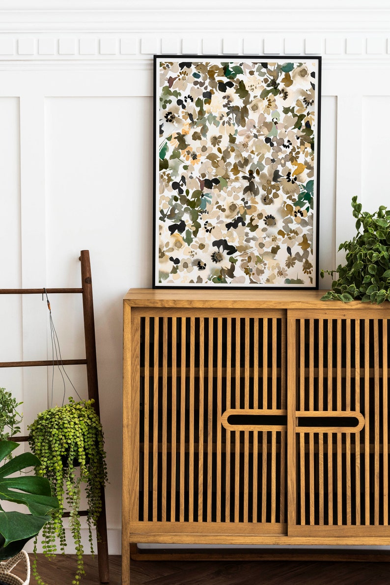 May include: A wooden cabinet with two doors and a black framed print of an abstract floral design hanging above it. The cabinet has a slatted design and is made of light brown wood. The print is a watercolor style with a white background and brown, green, and yellow flowers.