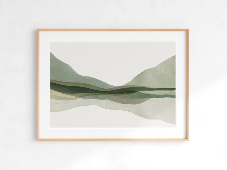 May include: A framed watercolor landscape print featuring layered green and olive-toned hills and a reflective body of water. The artwork is set against a neutral background and framed in a light wood frame, creating a serene and natural aesthetic.