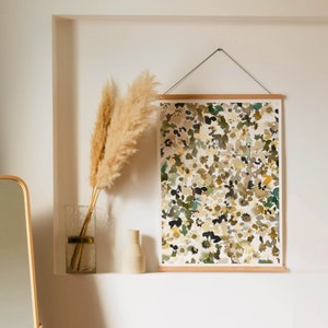 May include: A framed print of an abstract floral pattern in shades of brown, green, and white. The print is hanging on a white wall with a dried pampas grass arrangement in a clear glass vase.