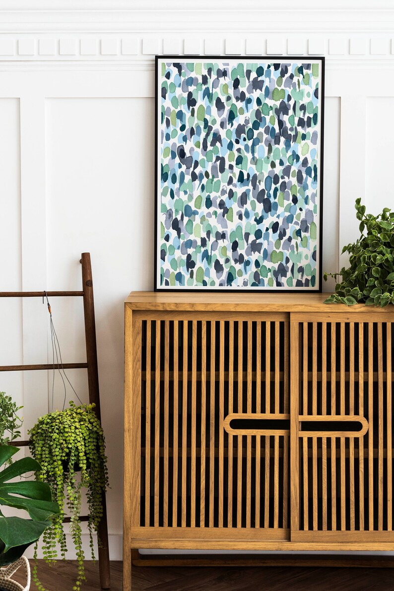 Puede incluir: Un armario de madera con dos puertas y una impresi&oacute;n enmarcada en negro de una pintura abstracta de acuarela con colores azules y verdes. El armario tiene un dise&ntilde;o de listones y est&aacute; sentado sobre una superficie blanca.