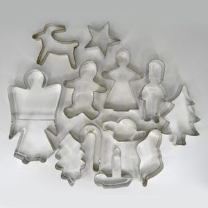 May include: A collection of twelve silver-toned metal cookie cutters in various shapes, including a star, a reindeer, a gingerbread person, an angel, a Christmas tree, a candy cane, a candle, and other holiday-themed silhouettes.