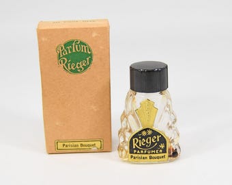 Puede incluir: Un frasco de perfume vintage con tapa negra y etiqueta decorativa, junto a una caja a juego. El frasco es transparente con una etiqueta dorada y negra que dice "Rieger Parfumer Parisian Bouquet". La caja es de color canela con las palabras "Parfum Rieger" en verde.