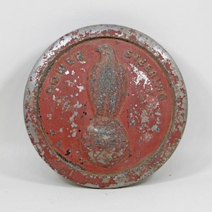 Puede incluir: Una tapa metálica redonda, roja y plateada, con las palabras "POWER STEERING" y "CASE" en relieve. La tapa presenta un diseño de águila en relieve. La pintura está desconchada, dándole un aspecto vintage.