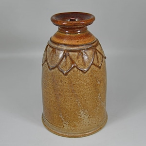 May include: A handcrafted ceramic vase with a textured, speckled surface. The vase features a flared rim and a decorative band of leaf-like patterns around the upper portion. The color palette includes shades of brown and tan.