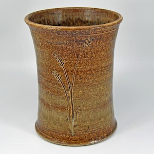 May include: A handcrafted ceramic vase with a rustic, textured appearance. The vase is primarily brown with lighter, earthy tones and features an etched botanical design. The cylindrical shape has a slightly flared rim. A decorative piece for home decor.