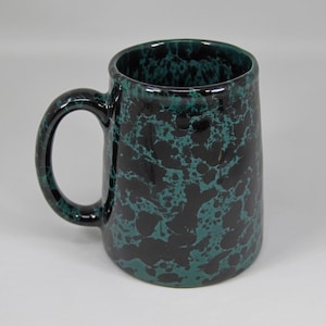 Può includere: Una tazza in ceramica con un motivo marmorizzato nero e verde acqua. La tazza ha un manico grande e una forma cilindrica. L'interno e il manico sono dello stesso colore verde acqua della marmorizzazione. La tazza è adatta per bevande calde o fredde.