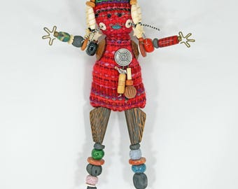 Puede incluir: Muñeca de arte popular hecha a mano con un vestido rojo tejido, piernas de madera y brazos y piernas con cuentas. La muñeca tiene un sombrero tejido colorido, cabello de madera y un colgante plateado. Un artículo decorativo único y artesanal.