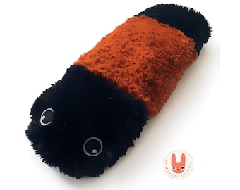 May include: A plush toy worm in black, orange, and black. The worm has two white eyes with black pupils. The toy is made of a soft, fuzzy material. The toy is on a white background.