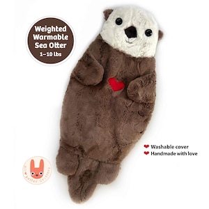 May include: A plush sea otter toy with brown fur, a cream-colored face, black eyes, and a red heart patch on its chest. Text reads: Weighted Warmable Sea Otter 1-10 lbs, Washable cover, Handmade with love. Includes an all better critters logo.
