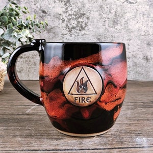 May include: A black and red ceramic mug with a white triangle and flame design. The mug says "FIRE" in the center of the triangle.