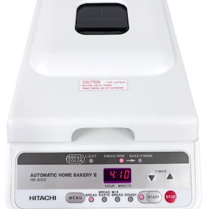 May include: A white Hitachi Automatic Home Bakery II bread maker, model HB-B102, featuring a digital display showing 4:10, a control panel with buttons for menu, start, and stop, and a caution label on the lid regarding hot surfaces.