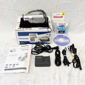 May include: A silver Panasonic DVD video camera with a black carrying pouch, a branded cardboard box, an instruction manual, a battery charger, multiple black power cables, a pack of four Maxell DVD-RW discs, and a single Panasonic DVD-RW disc.