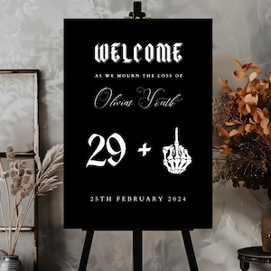 Peut inclure: Une pancarte d'accueil noire avec du texte blanc qui dit "Welcome as we mourn the loss of Olivia's Youth 29 +" avec une main squelettique faisant un doigt d'honneur et la date "25th February 2024".