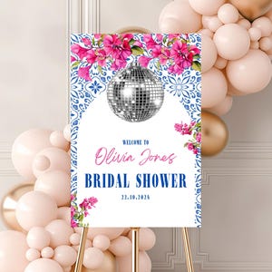 Puede incluir: Un cartel de bienvenida blanco con patrones florales azules y blancos y una bola de discoteca plateada. El cartel dice "Bienvenido a Olivia Jones Bridal Shower 22.10.2024".