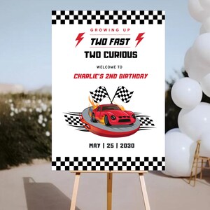 May include: A white sign with a black and white checkered border. The sign says "Growing Up Two Fast Two Curious" and "Welcome to Charlie's 2nd Birthday". The sign also has a red race car with flames and checkered flags. The date May 25, 2030 is printed at the bottom of the sign.