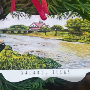May include: White ceramic ornament with a watercolor painting of a small town with a bridge over a river. The text "SALADO, TEXAS" is printed at the bottom of the ornament.