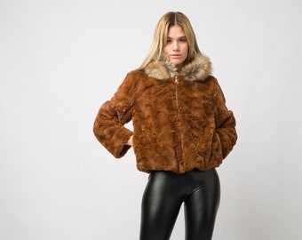 May include: A brown faux fur jacket with a zipper closure and a hood lined with brown faux fur. The jacket is worn over black leggings and black ankle boots.
