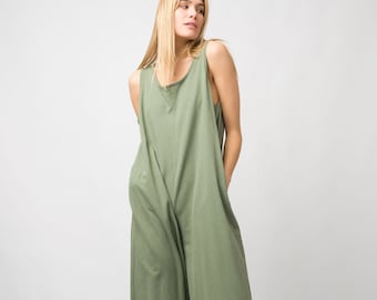 May include: A woman wearing a green sleeveless jumpsuit with pockets and black ankle boots.