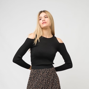 Op de afbeelding: Een zwart lang mouw shirt met uitgesneden schouders en een geribbelde textuur. Het shirt is gecombineerd met een zwart en bruin gepatroneerde rok.