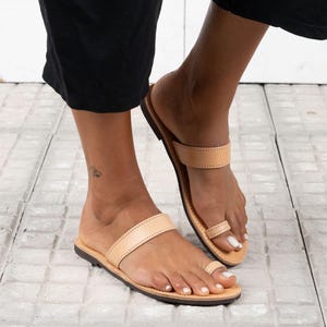 May include: A pair of tan leather thong sandals with a single strap across the top of the foot. The sandals have a simple design and are perfect for warm weather.