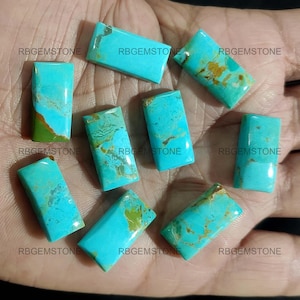Puede incluir: Nueve cabujones de turquesa en varios tonos de azul y verde, con inclusiones marrones y doradas. Los cabujones son rectangulares y tienen una superficie lisa y pulida. Están dispuestos en una mano.
