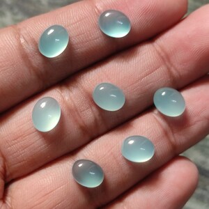 May include: Seven oval-shaped, light blue gemstones. The gemstones are smooth and polished.