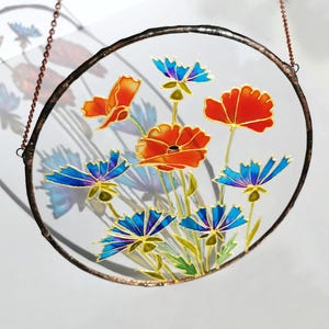 May include: A round stained glass window hanging with a copper chain. The window features a floral design with red poppies and blue cornflowers.