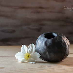 Può includere: Una tazza di ceramica bianca con manico nero e la scritta "But First, Coffee" in grassetto nero. La tazza è appoggiata su una superficie bianca. La tazza è alta circa 10 cm.