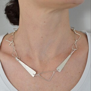 May include: A silver necklace with a geometric design featuring triangular links and long, flat, triangular pendants.