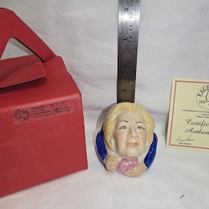 Puede incluir: Busto de cerámica de Margaret Thatcher con cabello rubio, chaqueta azul y pajarita rosa. El busto va acompañado de una caja roja y un certificado de autenticidad. El busto mide aproximadamente 7.6 cm de altura.