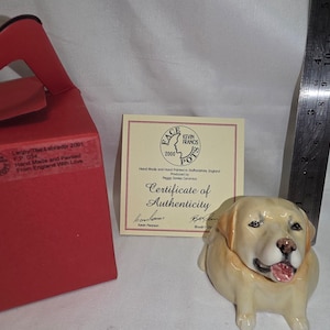 May include: A ceramic yellow Labrador retriever figurine, a red box, and a certificate of authenticity. A metal ruler shows the figurine is approximately 3 inches tall. The certificate features the text Face Pots Kevin Francis 2000 and Certificate of Authenticity. The box has a label with the text Labrador 2001 F.P. 054 Hand Made and Painted From England With Love.